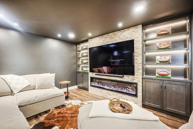 cinema with hardwood / wood-style flooring, a stone fireplace, and built in shelves