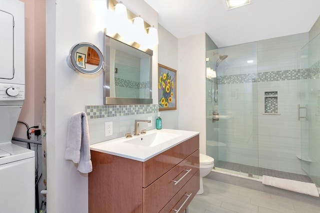 bathroom with backsplash, a shower stall, stacked washing maching and dryer, vanity, and toilet
