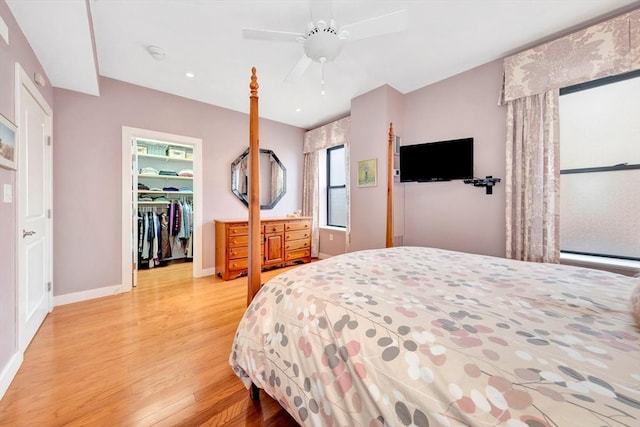 bedroom featuring a walk in closet, baseboards, light wood finished floors, and ceiling fan