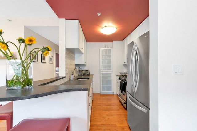 kitchen featuring a sink, light wood-style flooring, stainless steel appliances, white cabinetry, and a peninsula