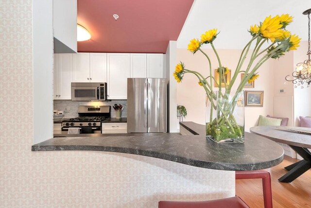 kitchen with decorative backsplash, dark countertops, wood finished floors, stainless steel appliances, and white cabinetry