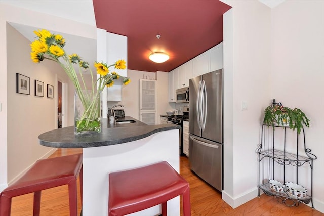 kitchen with a peninsula, dark countertops, a kitchen bar, a sink, and appliances with stainless steel finishes