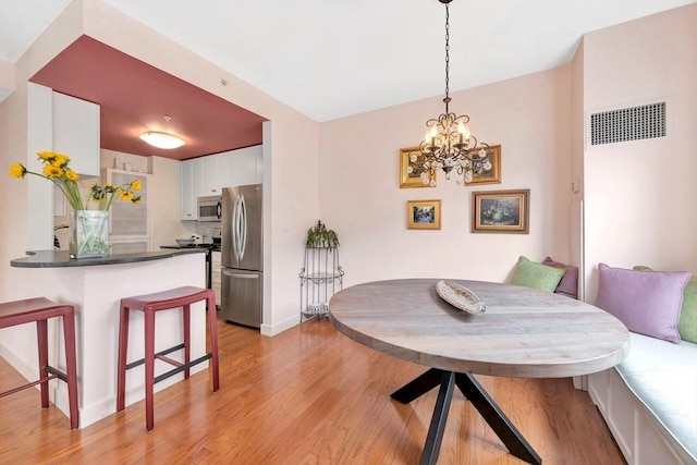 dining area featuring baseboards, a chandelier, light wood-style flooring, and visible vents