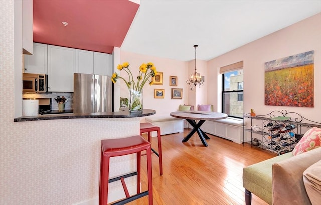 kitchen featuring appliances with stainless steel finishes, white cabinets, a peninsula, a chandelier, and light wood-style floors