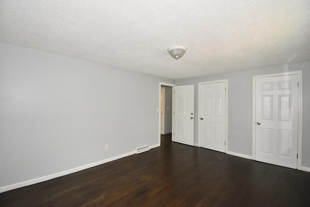 unfurnished bedroom featuring baseboards, dark wood-style floors, a textured ceiling, and visible vents
