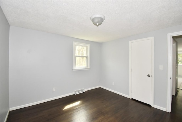 unfurnished room with a textured ceiling, baseboards, visible vents, and dark wood-style floors