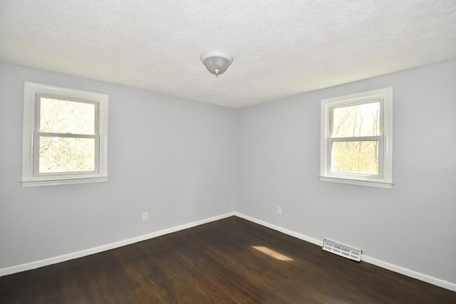 spare room featuring baseboards, dark wood finished floors, a textured ceiling, and visible vents