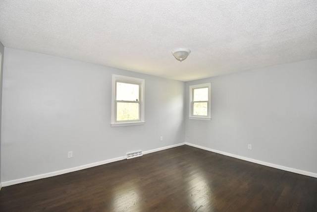 spare room featuring visible vents, a textured ceiling, dark wood finished floors, and baseboards
