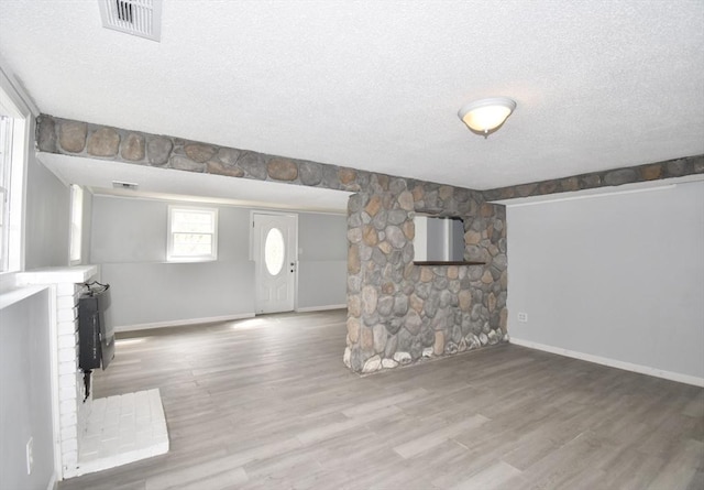 unfurnished living room featuring baseboards, a textured ceiling, visible vents, and wood finished floors