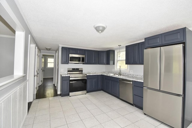 kitchen with light tile patterned flooring, light stone countertops, appliances with stainless steel finishes, a sink, and a textured ceiling
