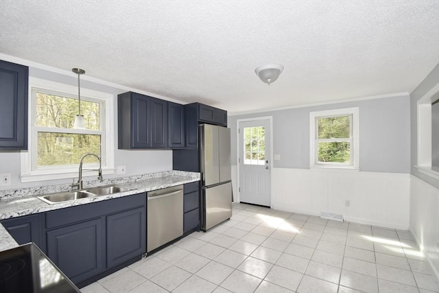 kitchen with a textured ceiling, decorative light fixtures, wainscoting, a sink, and stainless steel appliances