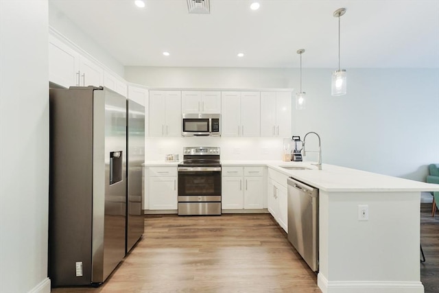 kitchen with appliances with stainless steel finishes, a sink, a peninsula, light wood-style flooring, and recessed lighting
