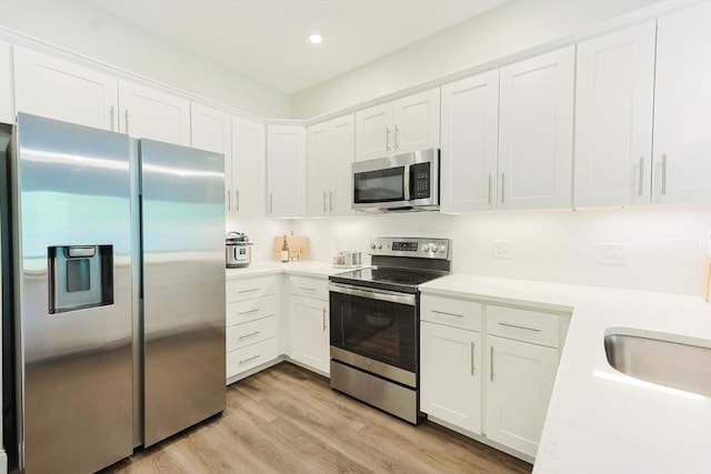 kitchen featuring stainless steel appliances, light countertops, white cabinetry, decorative backsplash, and light wood finished floors