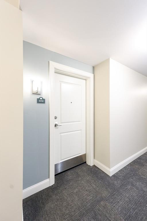 corridor featuring dark colored carpet and baseboards