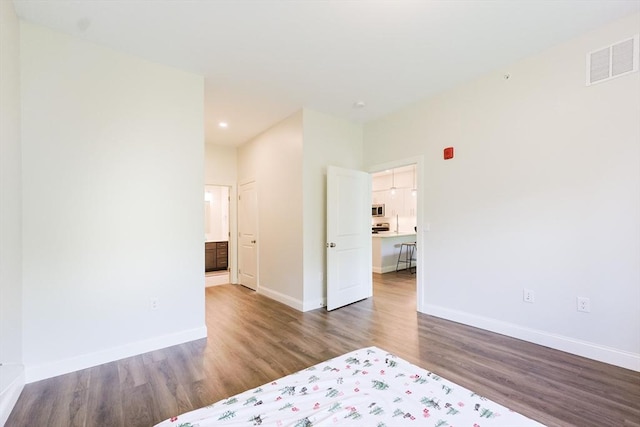 unfurnished bedroom featuring wood finished floors, baseboards, recessed lighting, and ensuite bathroom