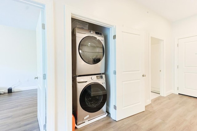 laundry area featuring stacked washer / drying machine, light wood-style flooring, and baseboards