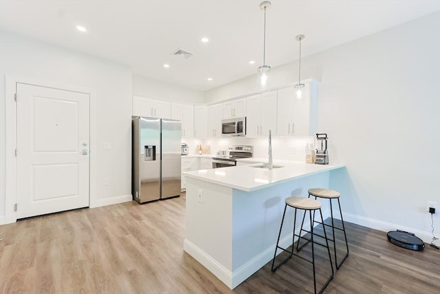 kitchen with stainless steel appliances, a peninsula, a sink, a breakfast bar area, and light wood-style floors