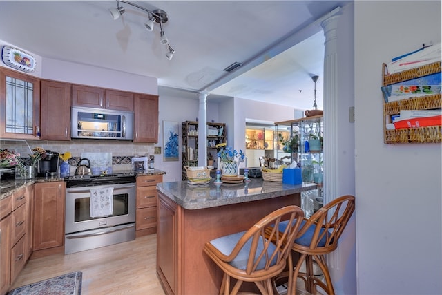 kitchen with a breakfast bar, appliances with stainless steel finishes, a kitchen island, and ornate columns