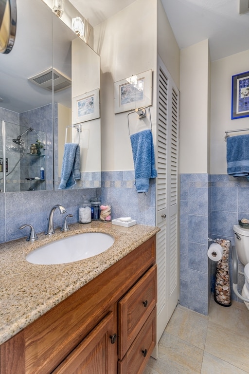 bathroom featuring a tile shower, tile walls, vanity, and toilet