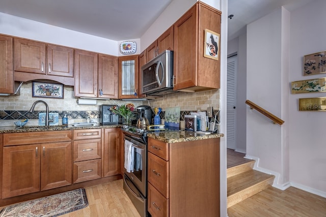 kitchen featuring appliances with stainless steel finishes, dark stone countertops, tasteful backsplash, light hardwood / wood-style flooring, and sink