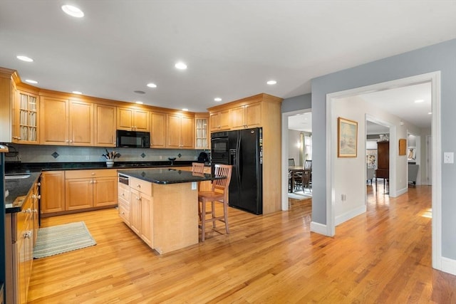 kitchen featuring a kitchen bar, black appliances, light wood-type flooring, a kitchen island, and backsplash