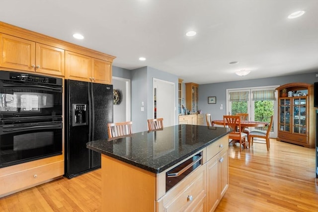 kitchen with a kitchen island, light hardwood / wood-style flooring, dark stone counters, and black appliances