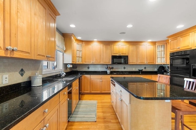 kitchen with a kitchen island, a breakfast bar area, dark stone counters, and black appliances