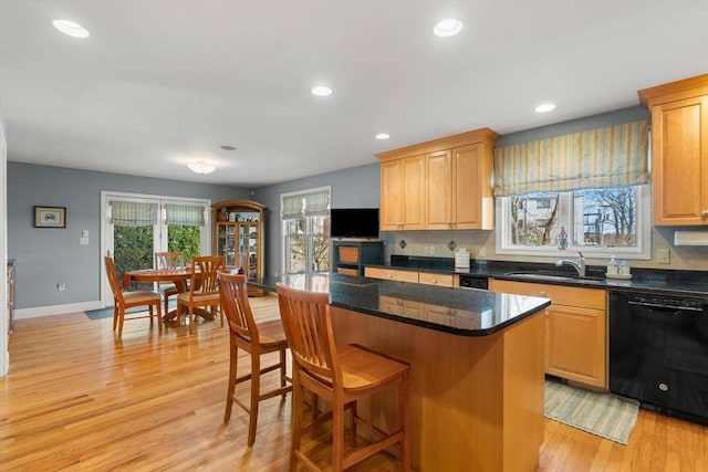 kitchen featuring black dishwasher, dark stone countertops, sink, a center island, and light hardwood / wood-style floors