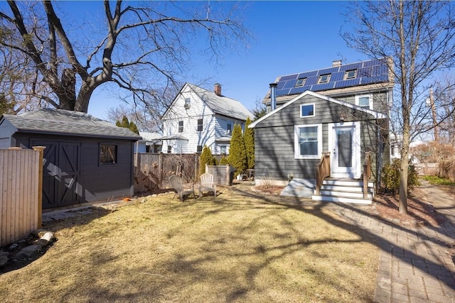 back of house with entry steps, a shed, fence, an outdoor structure, and solar panels