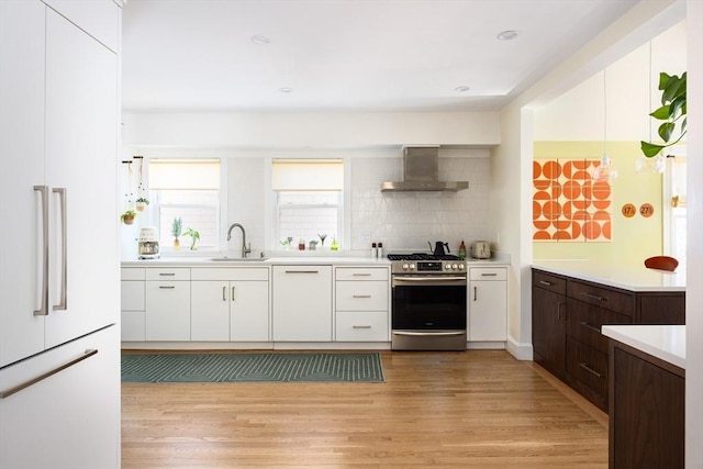 kitchen with a sink, light wood finished floors, paneled appliances, and wall chimney range hood