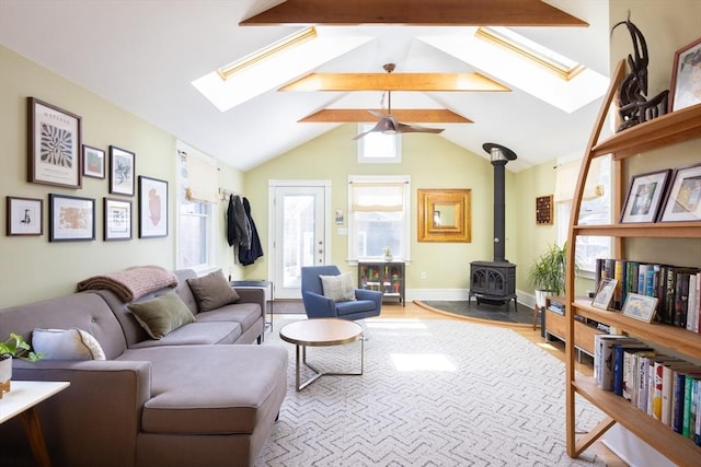 living room with baseboards, vaulted ceiling with skylight, wood finished floors, and a wood stove