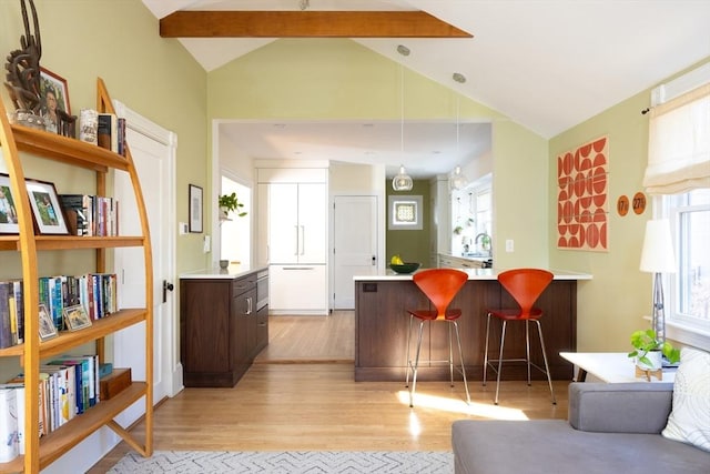 kitchen featuring light wood finished floors, lofted ceiling with beams, light countertops, dark brown cabinets, and a kitchen breakfast bar