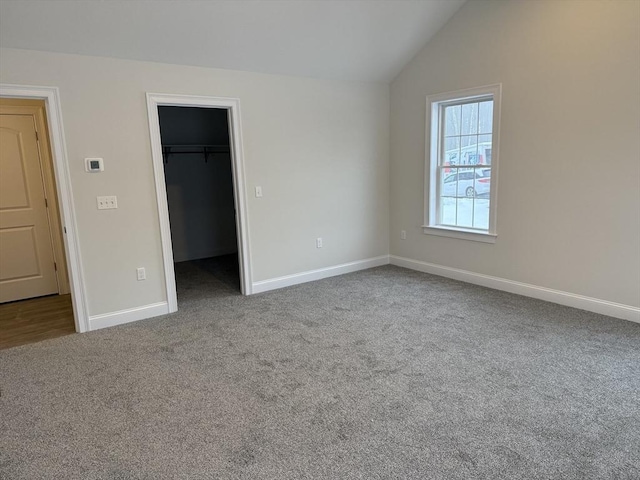 unfurnished bedroom with baseboards, carpet, a spacious closet, vaulted ceiling, and a closet