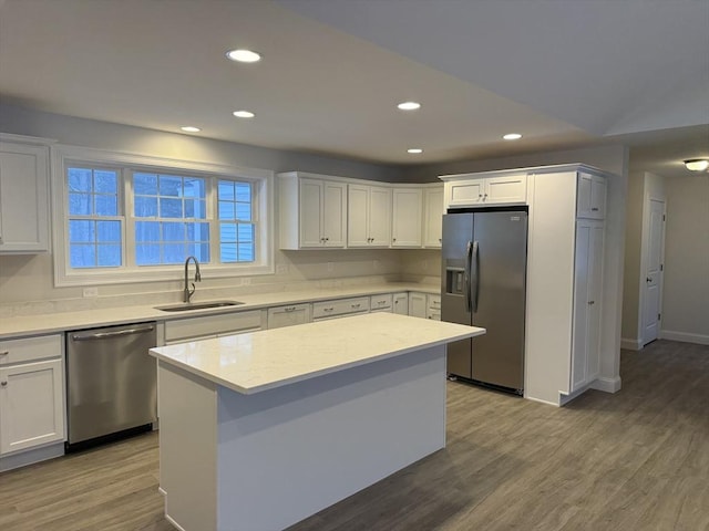 kitchen with light wood finished floors, appliances with stainless steel finishes, light countertops, white cabinetry, and a sink