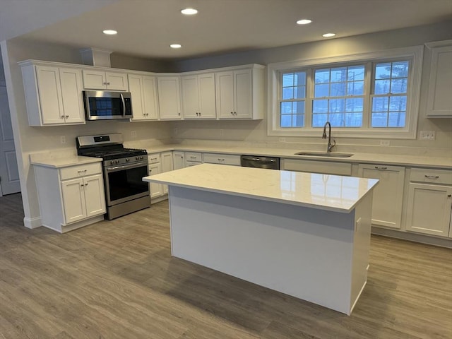 kitchen with light countertops, appliances with stainless steel finishes, white cabinets, a sink, and wood finished floors