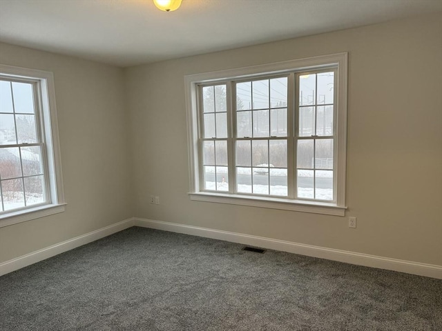 spare room featuring baseboards, visible vents, and dark carpet