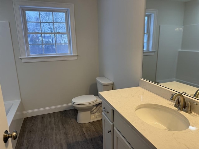 bathroom featuring a washtub, toilet, wood finished floors, vanity, and baseboards