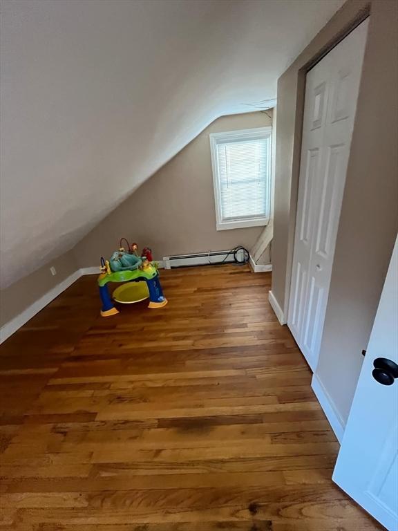 additional living space featuring vaulted ceiling, hardwood / wood-style flooring, and a baseboard radiator