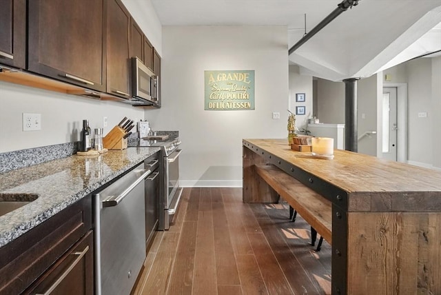 kitchen featuring appliances with stainless steel finishes, decorative columns, dark brown cabinets, light stone countertops, and dark wood-type flooring