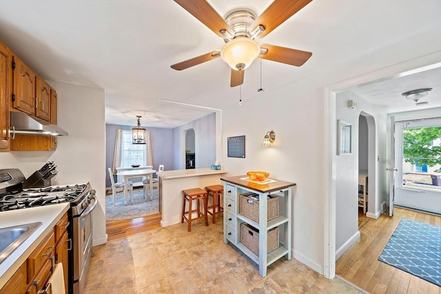 40 Mamie Rd, Weymouth, MA 02190 - kitchen featuring gas range, arched walkways, under cabinet range hood, brown cabinetry, and a ceiling fan