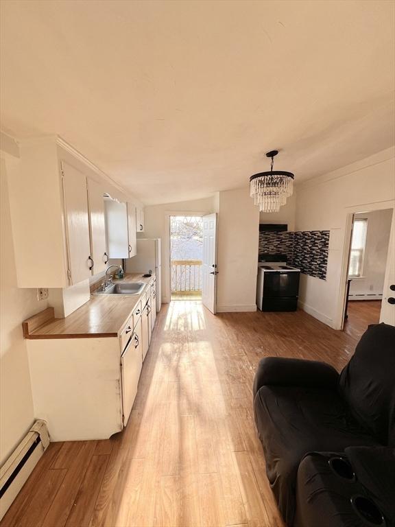 kitchen with a baseboard radiator, light countertops, light wood-style floors, white cabinetry, and a sink