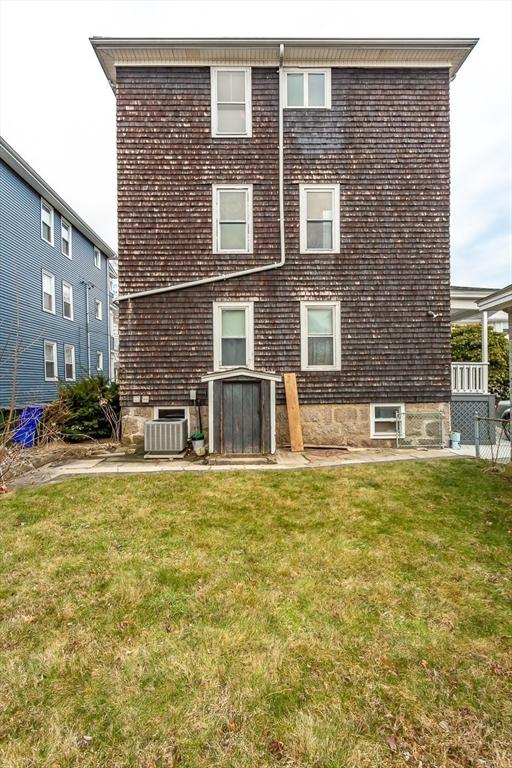 rear view of property featuring cooling unit and a lawn