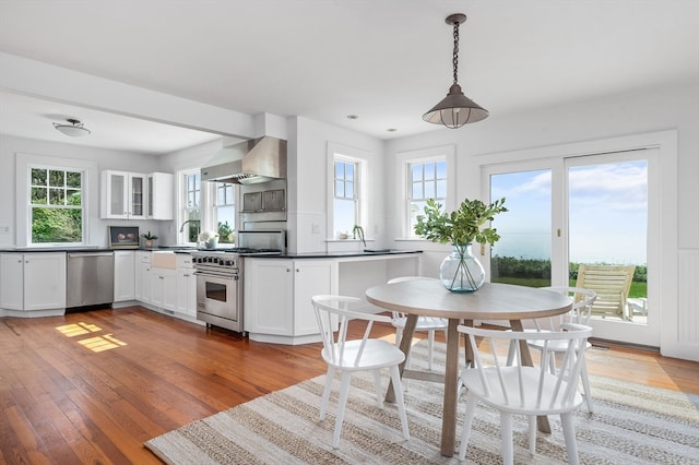 kitchen with a wealth of natural light, stainless steel appliances, wall chimney range hood, and white cabinetry