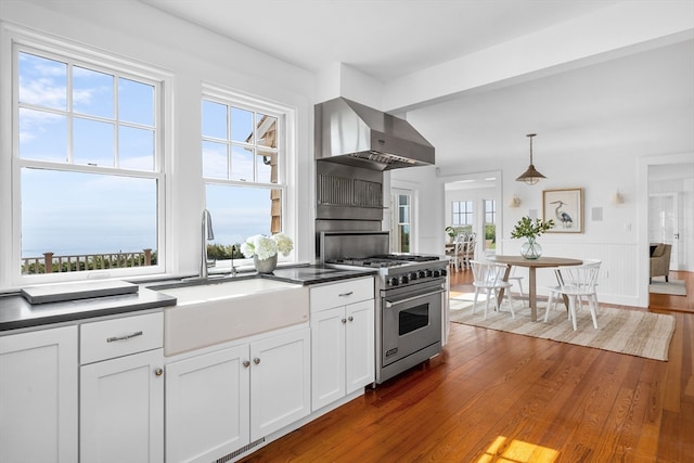 kitchen featuring wall chimney exhaust hood, high end stove, hanging light fixtures, and a healthy amount of sunlight