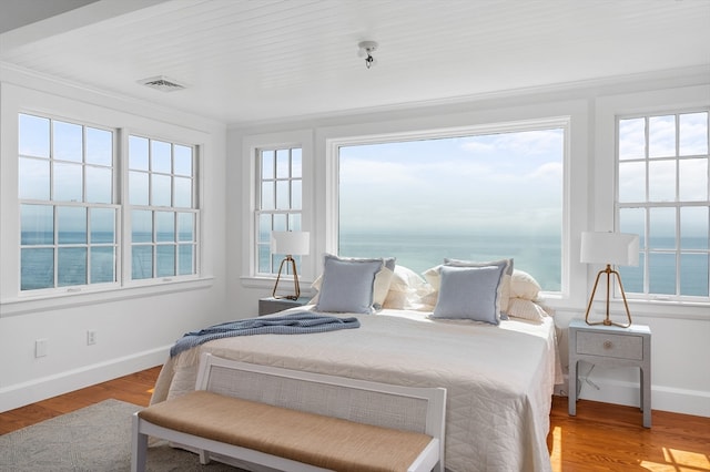 bedroom with wood-type flooring, a water view, and multiple windows