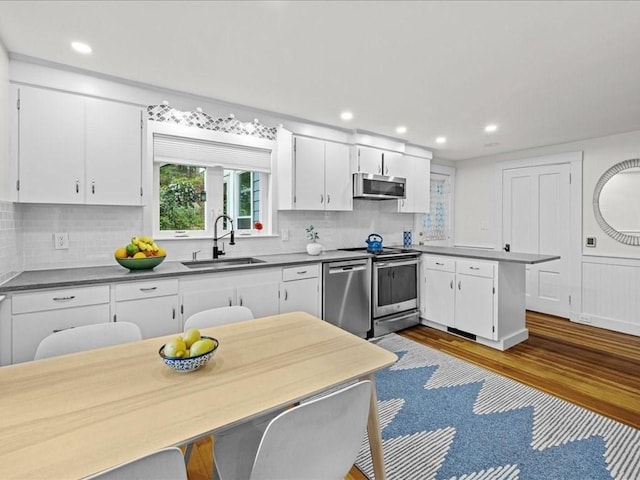 kitchen featuring a sink, stainless steel appliances, a peninsula, white cabinetry, and recessed lighting