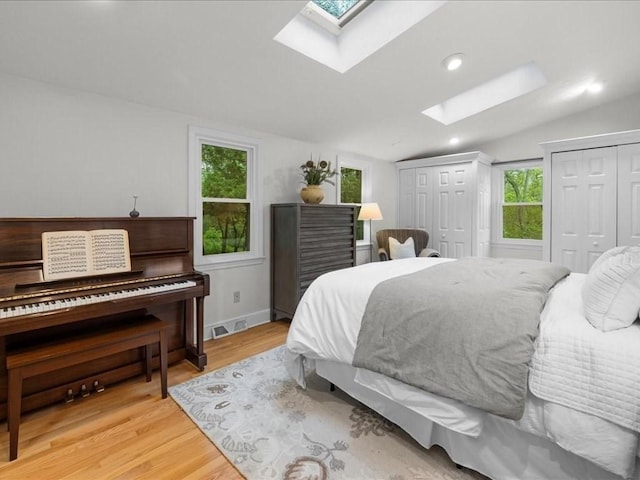 bedroom with a skylight, two closets, vaulted ceiling, light wood-style flooring, and recessed lighting