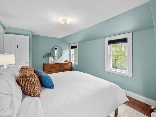 bedroom featuring wood finished floors, multiple windows, baseboards, and lofted ceiling