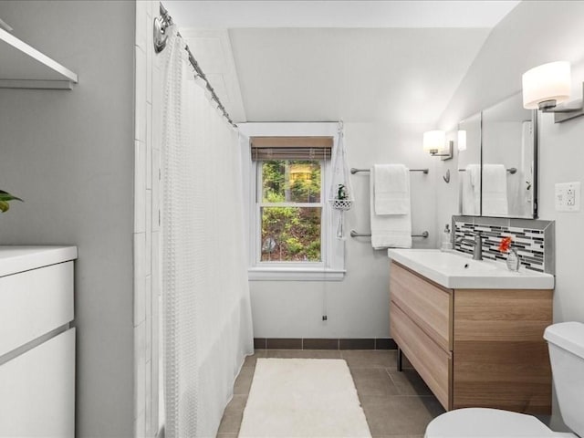 bathroom featuring vanity, toilet, tile patterned flooring, backsplash, and vaulted ceiling