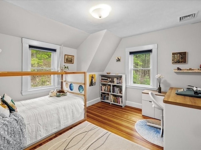 bedroom with multiple windows, wood finished floors, baseboards, lofted ceiling, and a desk